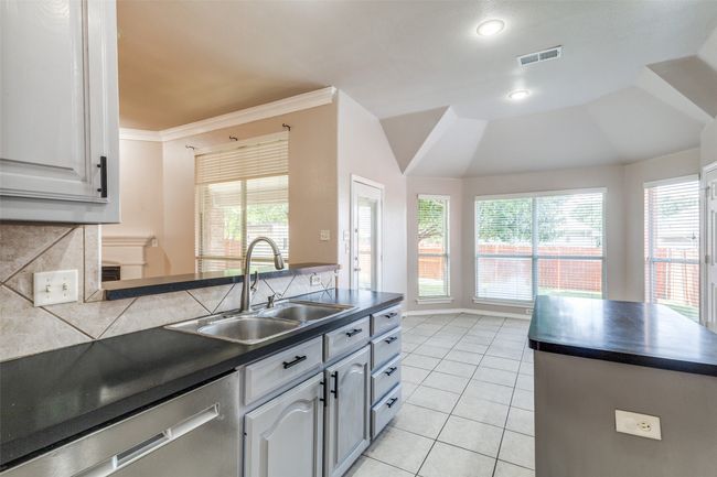Kitchen featuring dark countertops, stainless steel dishwasher, light tile patterned flooring, a peninsula, and ornamental molding | Image 10
