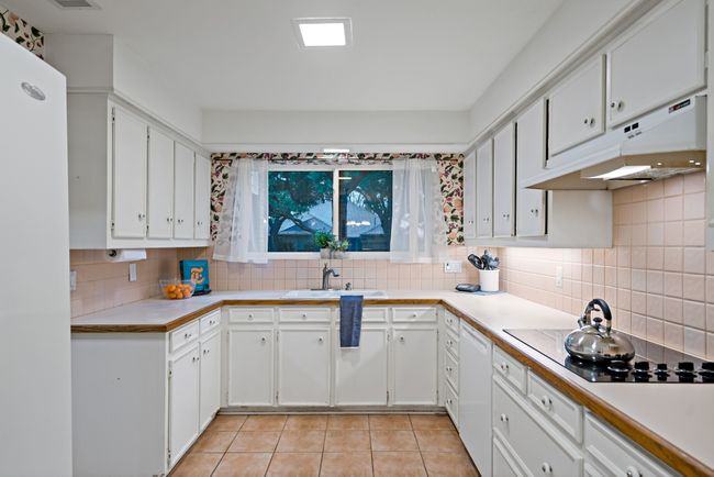 Kitchen with light tile flooring, white appliances, under cabinet range hood, tasteful backsplash, and a sink | Image 11