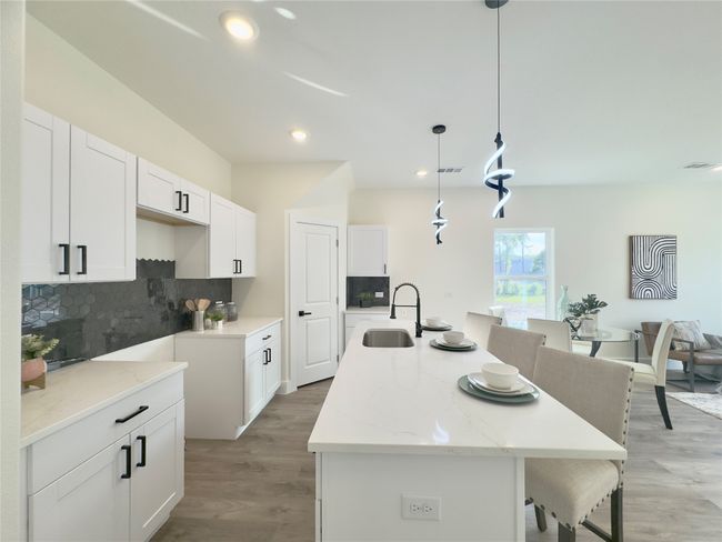 Kitchen featuring an island with sink, white cabinets, backsplash, a sink, and visible vents | Image 6