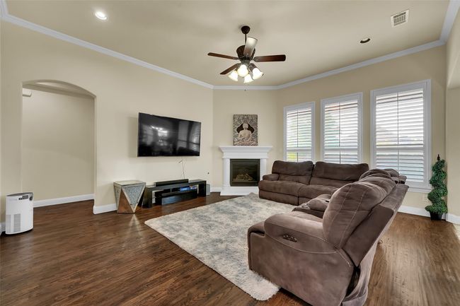 Living area with ornamental molding, arched walkways, dark wood finished floors, a glass covered fireplace, and ceiling fan | Image 14