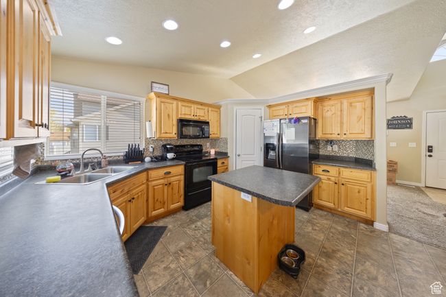 Kitchen featuring black appliances, vaulted ceiling, tasteful backsplash, dark countertops, and a center island | Image 7