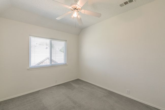 Empty room featuring a textured ceiling, baseboards, visible vents, a ceiling fan, and dark carpet | Image 15