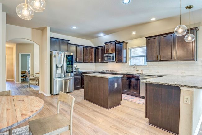 Kitchen featuring light stone countertops, arched walkways, dark brown cabinets, a sink, and stainless steel appliances | Image 11