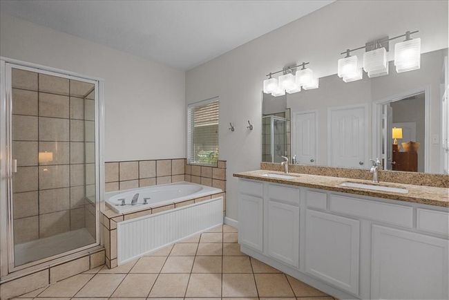 This primary bath features a spacious layout with a walk-in shower, a large soaking tub, dual sinks with granite countertops, and modern light fixtures. | Image 19