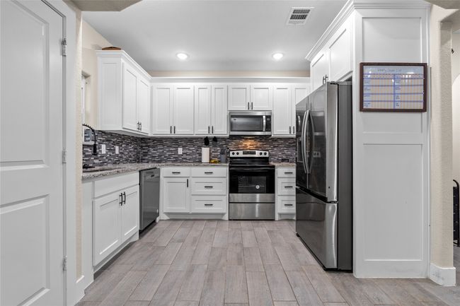 Kitchen featuring appliances with stainless steel finishes, white cabinetry, decorative backsplash, light wood-style floors, and light stone counters | Image 20