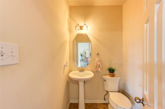 This is a compact, well-lit half bathroom featuring a pedestal sink, a toilet, a decorative mirror, and wall-mounted lighting. | Image 24