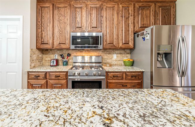 Kitchen with stainless steel appliances, brown cabinetry, tasteful backsplash, and light stone counters | Image 19