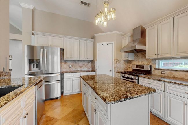 Kitchen featuring tasteful backsplash, visible vents, a center island, wall chimney range hood, and appliances with stainless steel finishes | Image 12