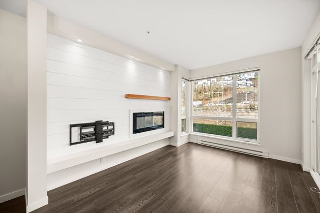 Unfurnished living room with a baseboard radiator, a fireplace, and dark wood-style floors | Image 8
