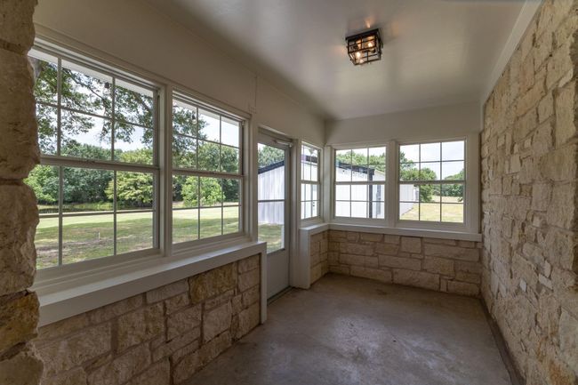Bright and inviting sunroom with charming stone walls and expansive windows, offering serene views of the lush outdoors. | Image 35