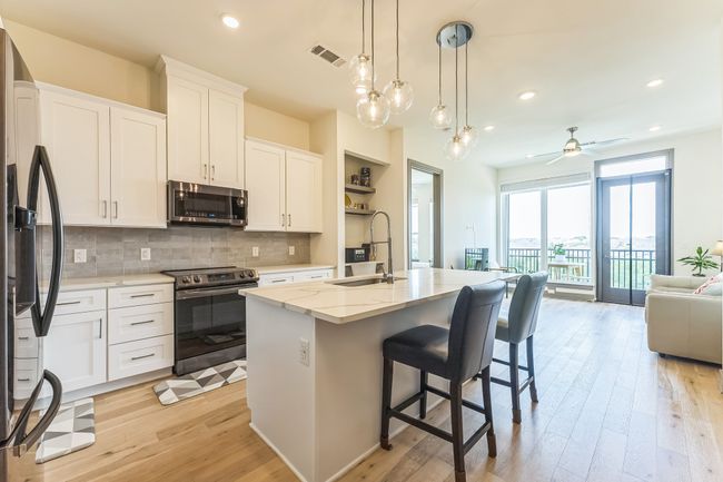 Kitchen with appliances with stainless steel finishes, open floor plan, light wood finished floors, white cabinetry, and light stone countertops | Image 9