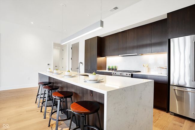 The kitchen has a pantry, large center island with soft close walnut drawers and cabinets, refrigerator with filtered water and ice, dishwasher, drawer microwave and beautiful quartz waterfall countertop | Image 6