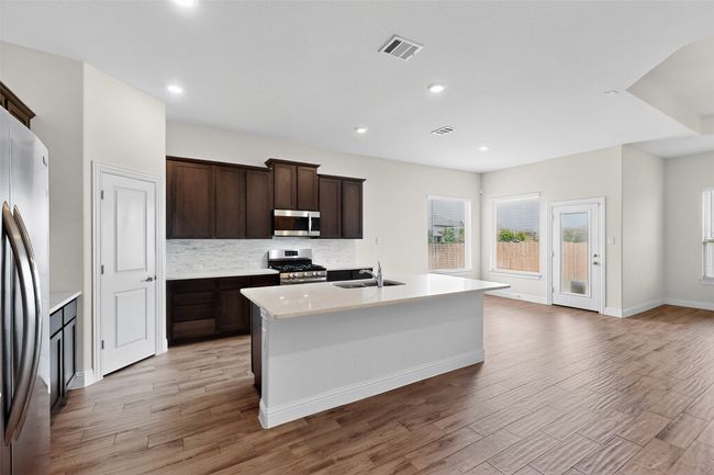 Kitchen featuring stainless steel appliances, light wood-type flooring, tasteful backsplash, an island with sink, and recessed lighting | Image 9