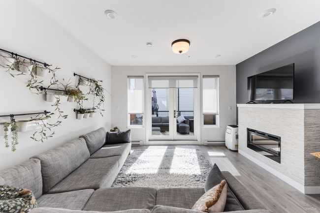 Living area featuring a glass covered fireplace, wood finished floors, baseboard heating, and baseboards | Image 5