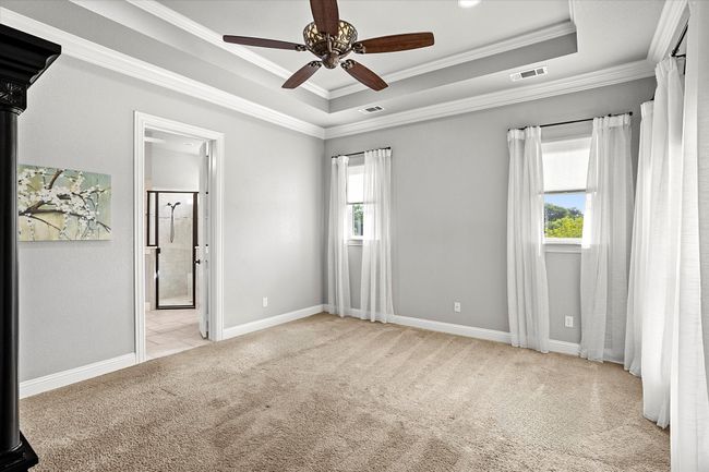 Unfurnished bedroom with light carpet, a tray ceiling, crown molding, ensuite bathroom, and ceiling fan | Image 16