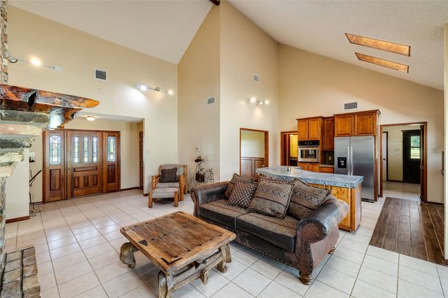 Living area with high vaulted ceiling, light tile patterned floors, a skylight, and baseboards | Image 4