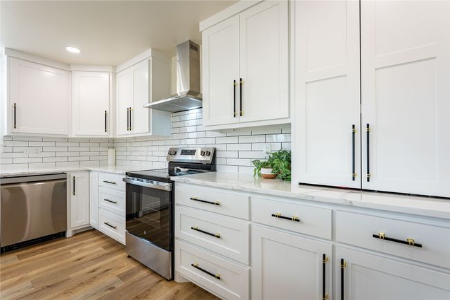 Kitchen featuring tasteful backsplash, light wood-style flooring, stainless steel appliances, wall chimney range hood, and white cabinetry | Image 6