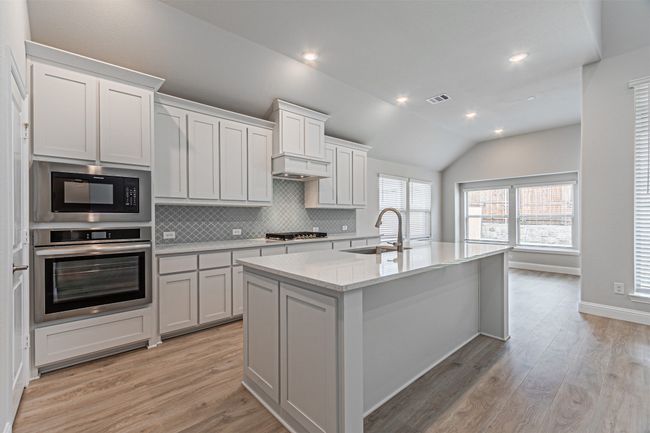 Kitchen with stainless steel appliances, backsplash, light wood-type flooring, a center island with sink, and vaulted ceiling | Image 15
