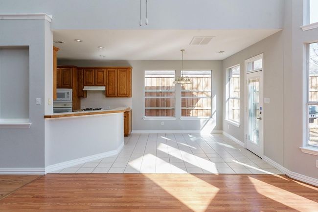 Kitchen with white appliances, visible vents, brown cabinetry, under cabinet range hood, and light tile patterned flooring | Image 9