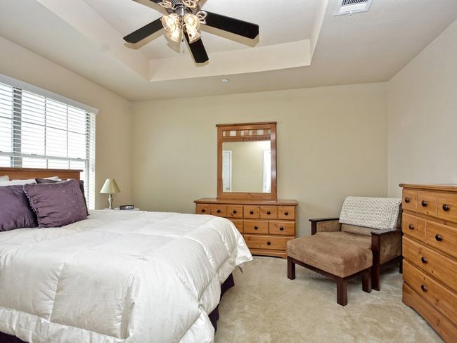 Bedroom featuring a tray ceiling, visible vents, light colored carpet, and ceiling fan | Image 16