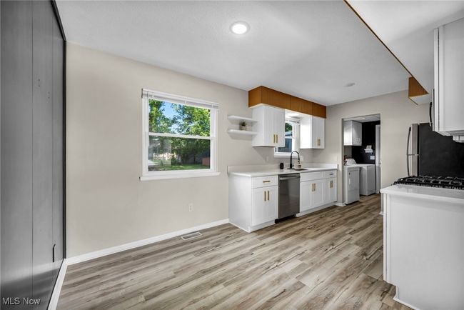 Kitchen featuring independent washer and dryer, stainless steel appliances, white cabinetry, light wood-type flooring, and light countertops | Image 23