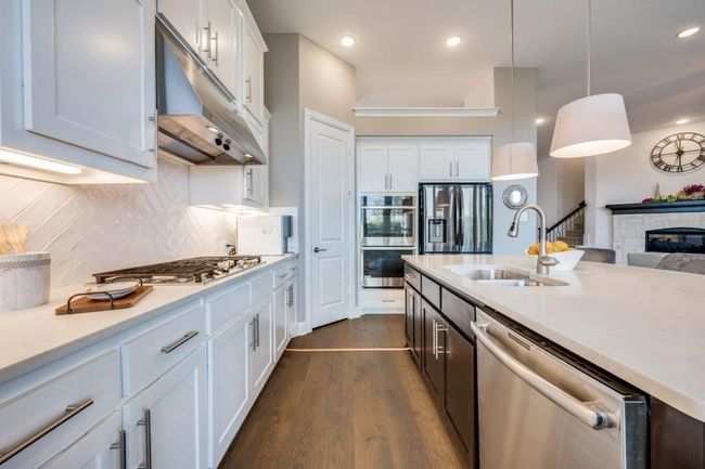 Kitchen featuring appliances with stainless steel finishes, under cabinet range hood, a sink, dark wood-type flooring, and a stone fireplace | Image 14