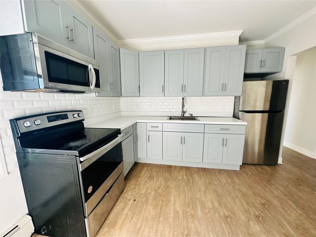 Kitchen featuring decorative backsplash, appliances with stainless steel finishes, ornamental molding, sink, and light hardwood / wood-style flooring | Image 4