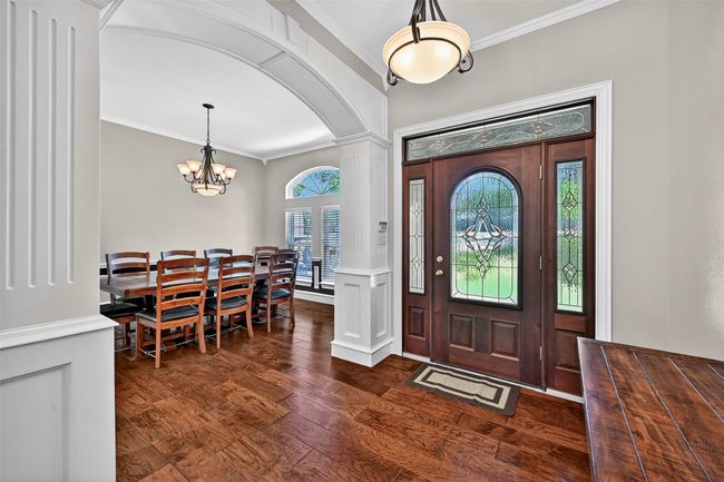 Entryway with crown molding, a chandelier, dark wood-style floors, arched walkways, and decorative columns | Image 7
