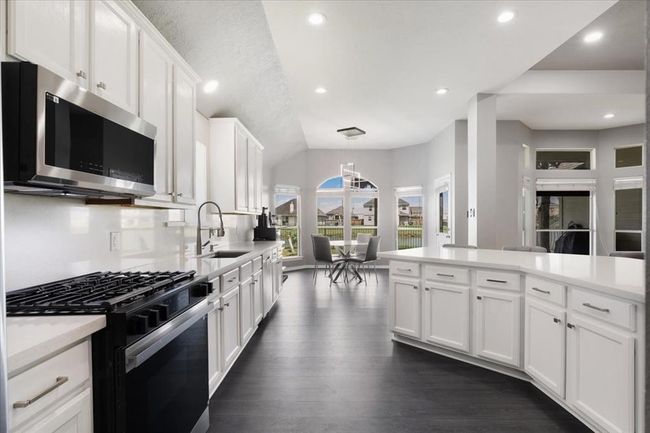 modern kitchen with sleek white cabinetry, stainless steel appliances, and a large island. The open layout extends to a bright dining area with large windows, offering plenty of natural light and views of the outdoors. | Image 6