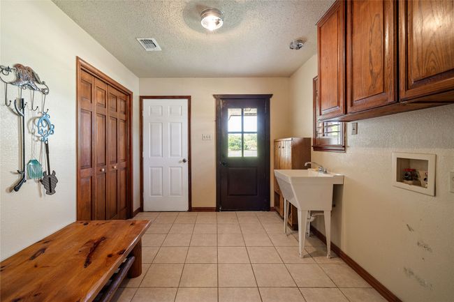 Washroom with hookup for a washing machine, cabinet space, a textured ceiling, light tile patterned flooring, and baseboards | Image 17