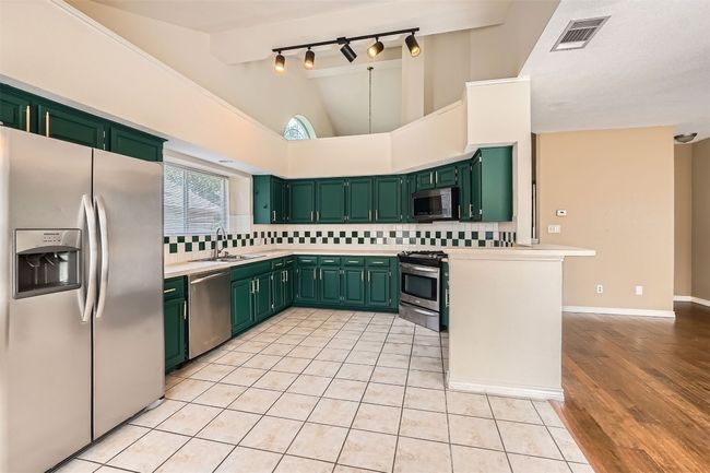 Kitchen featuring appliances with stainless steel finishes, green cabinetry, a sink, tasteful backsplash, and light countertops | Image 9
