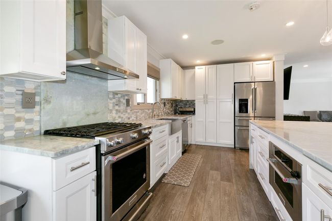 Kitchen featuring wall chimney range hood, crown molding, stainless steel appliances, dark wood-style floors, and light stone countertops | Image 10