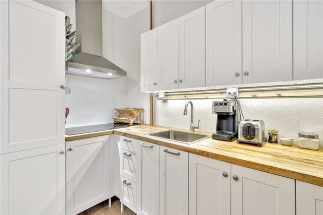 Kitchen with wall chimney exhaust hood, wooden counters, black electric stovetop, and white cabinets | Image 27