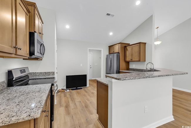Kitchen featuring appliances with stainless steel finishes, light wood finished floors, brown cabinets, a peninsula, and light stone counters | Image 13