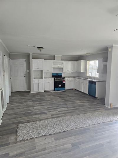 Kitchen with stainless steel stove, dark hardwood / wood-style flooring, dishwashing machine, and white cabinetry | Image 3