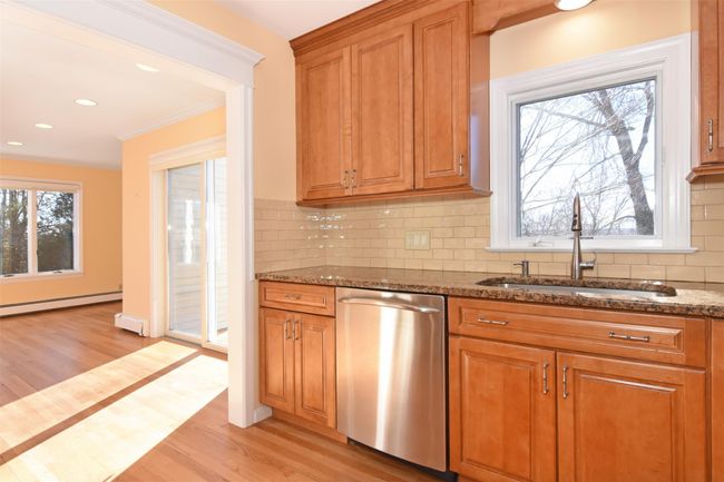 Kitchen with a baseboard heating unit, dishwasher, dark stone counters, light wood-type flooring, and a sink | Image 10