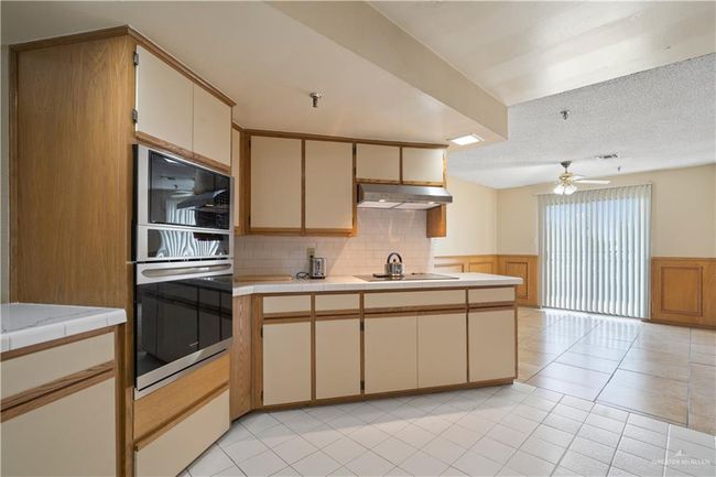 Kitchen with black appliances, under cabinet range hood, a wainscoted wall, tile counters, and cream cabinets | Image 8