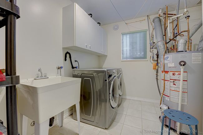 Laundry area with light tile patterned floors, baseboards, water heater, separate washer and dryer, and cabinet space | Image 14