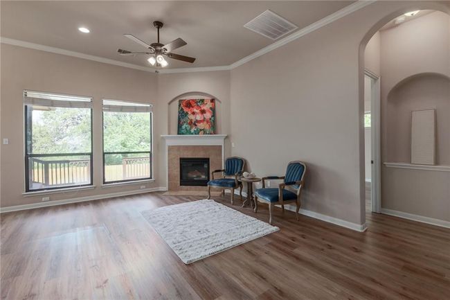 Living area featuring wood finished floors, a ceiling fan, arched walkways, a fireplace, and ornamental molding | Image 4
