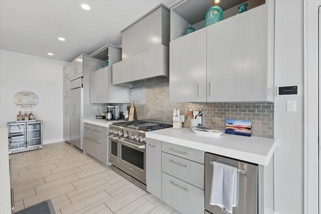 Kitchen featuring backsplash, range with two ovens, gray cabinetry, light countertops, and custom range hood | Image 16