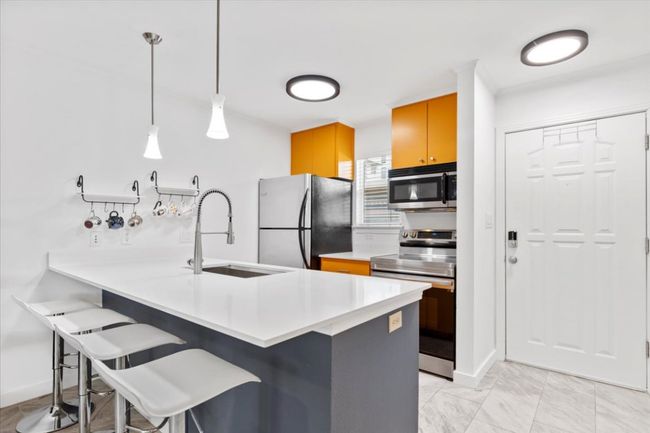 Kitchen with appliances with stainless steel finishes, a breakfast bar, a peninsula, light countertops, and decorative light fixtures | Image 6