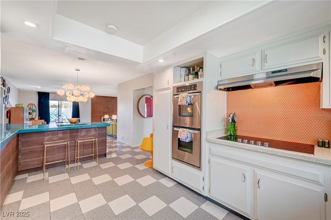 Kitchen with light floors, stainless steel double oven, black electric cooktop, and under cabinet range hood | Image 20