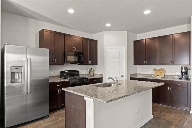 Kitchen featuring black appliances, a sink, dark wood finished floors, dark brown cabinets, and light stone counters | Image 13