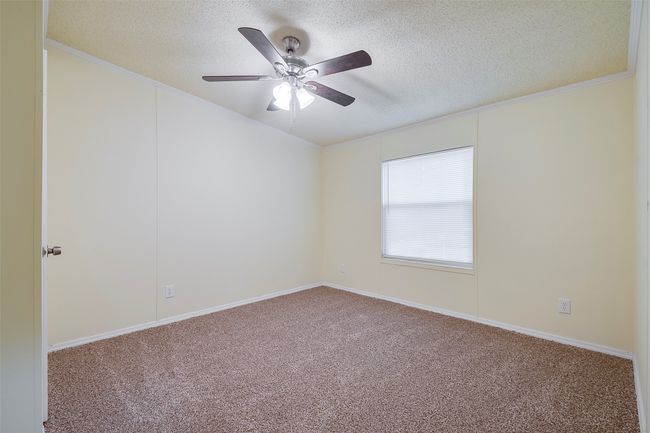 Carpeted empty room with a textured ceiling, ornamental molding, a ceiling fan, and vaulted ceiling | Image 12