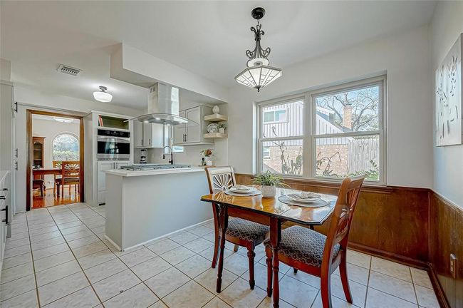 Bright kitchen with modern appliances, a cozy dining nook, and ample natural light from large windows. Features a tile floor and a view into the dining room with wood accents. | Image 14