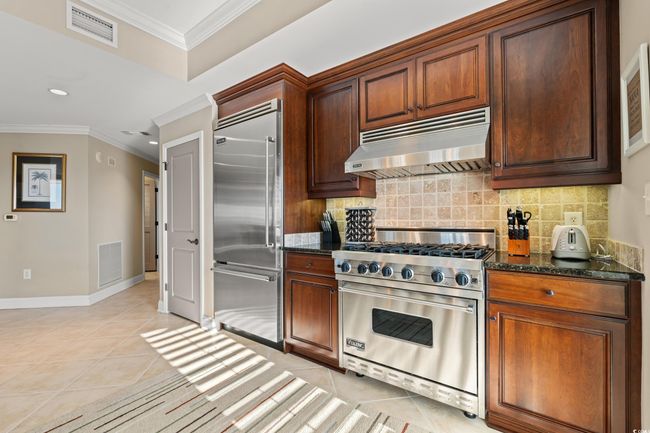 Kitchen with high quality appliances, light tile patterned floors, ornamental molding, backsplash, and under cabinet range hood | Image 19