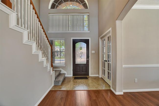 Bright and inviting entryway with high ceilings, featuring a stylish dark front door with decorative glass, elegant staircase, hardwood flooring, and access to a room with French doors. | Image 6