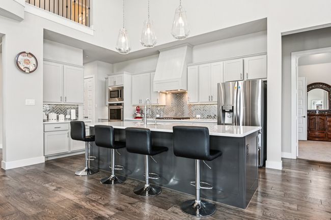 Kitchen featuring stainless steel appliances, dark wood-type flooring, light countertops, a breakfast bar area, and a high ceiling | Image 11