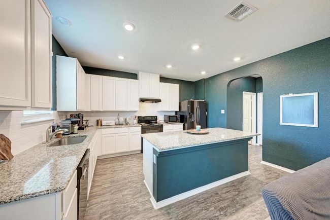 Kitchen featuring appliances with stainless steel finishes, a center island, arched walkways, light wood-style floors, and white cabinets | Image 17