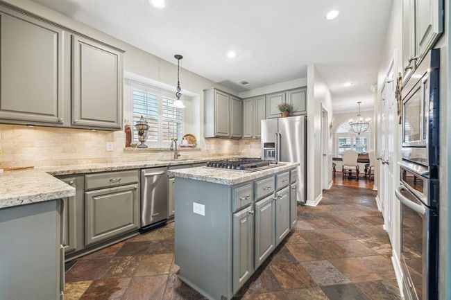 Experience gourmet cooking in a kitchen featuring sleek granite countertops, top-of-the-line stainless steel appliances, and a convenient island gas cooktop. | Image 13